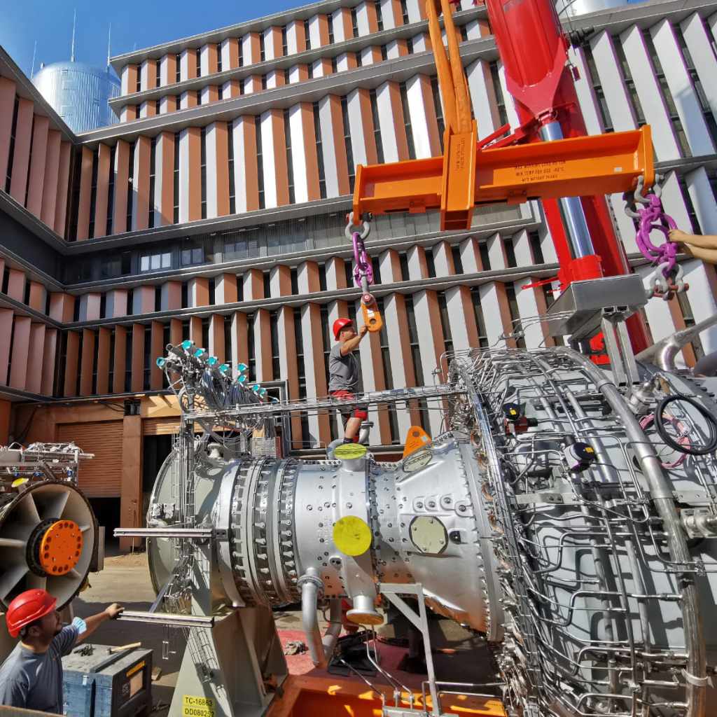 Autokran hebt eine Gasturbine vor einem Gebäude in Position